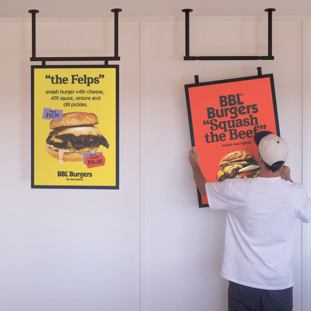 two black poster hanging menu boards installed side by side with person holding and hanging one up