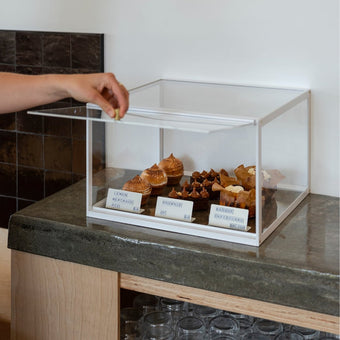 Small bakery display case on café counter with the lid being lifted to access pastries inside