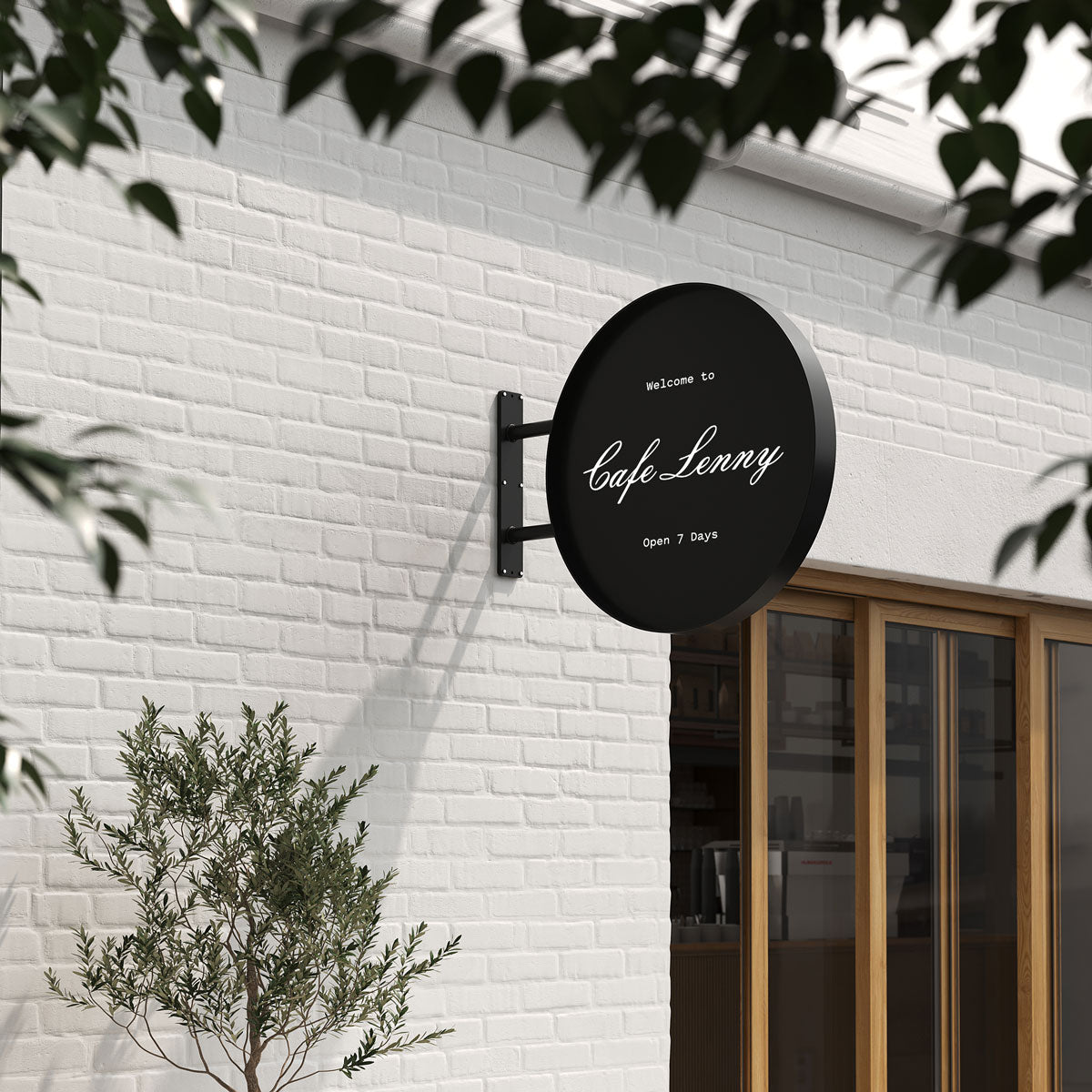 Big round wall sign in black finish with café logo, fixed on white brick wall with greenery