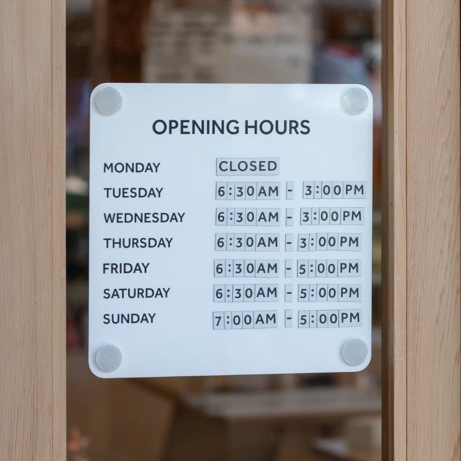 business hours of operation sign mounted on glass door advertising business hours in white steel panel