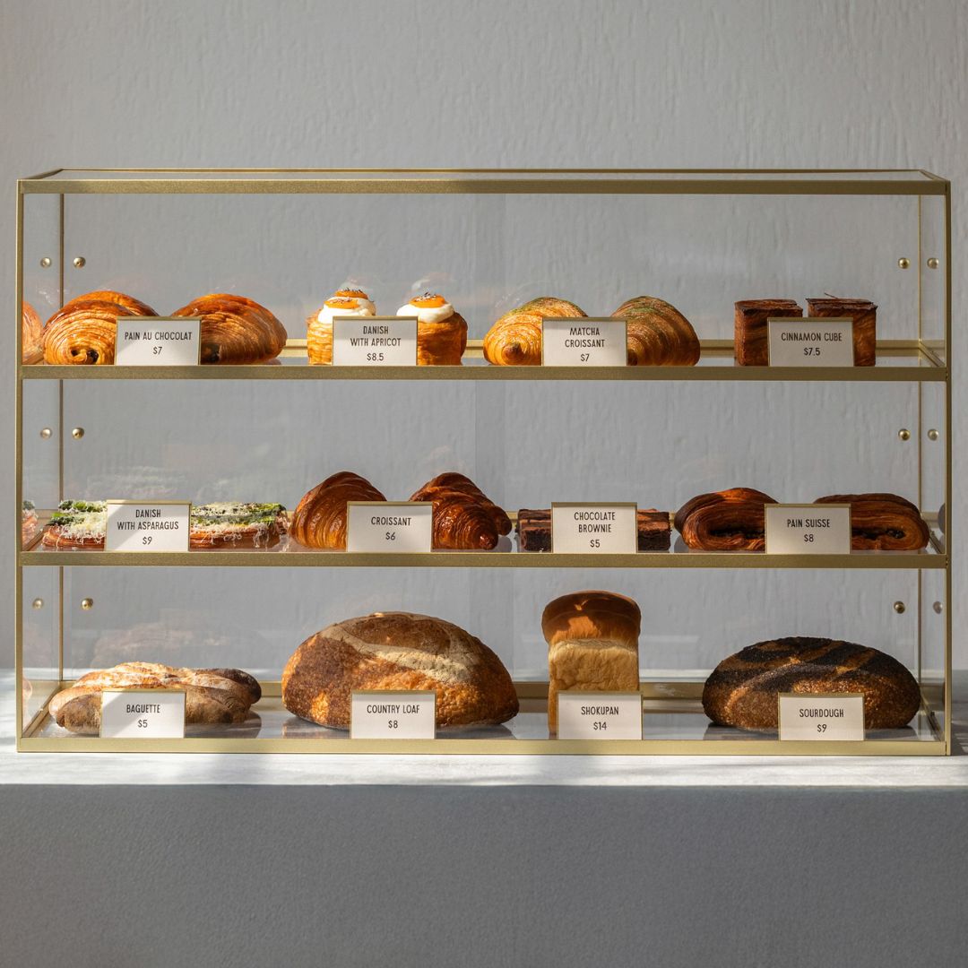 card counter signs in a three-tier bakery display case showing names and prices of pastries