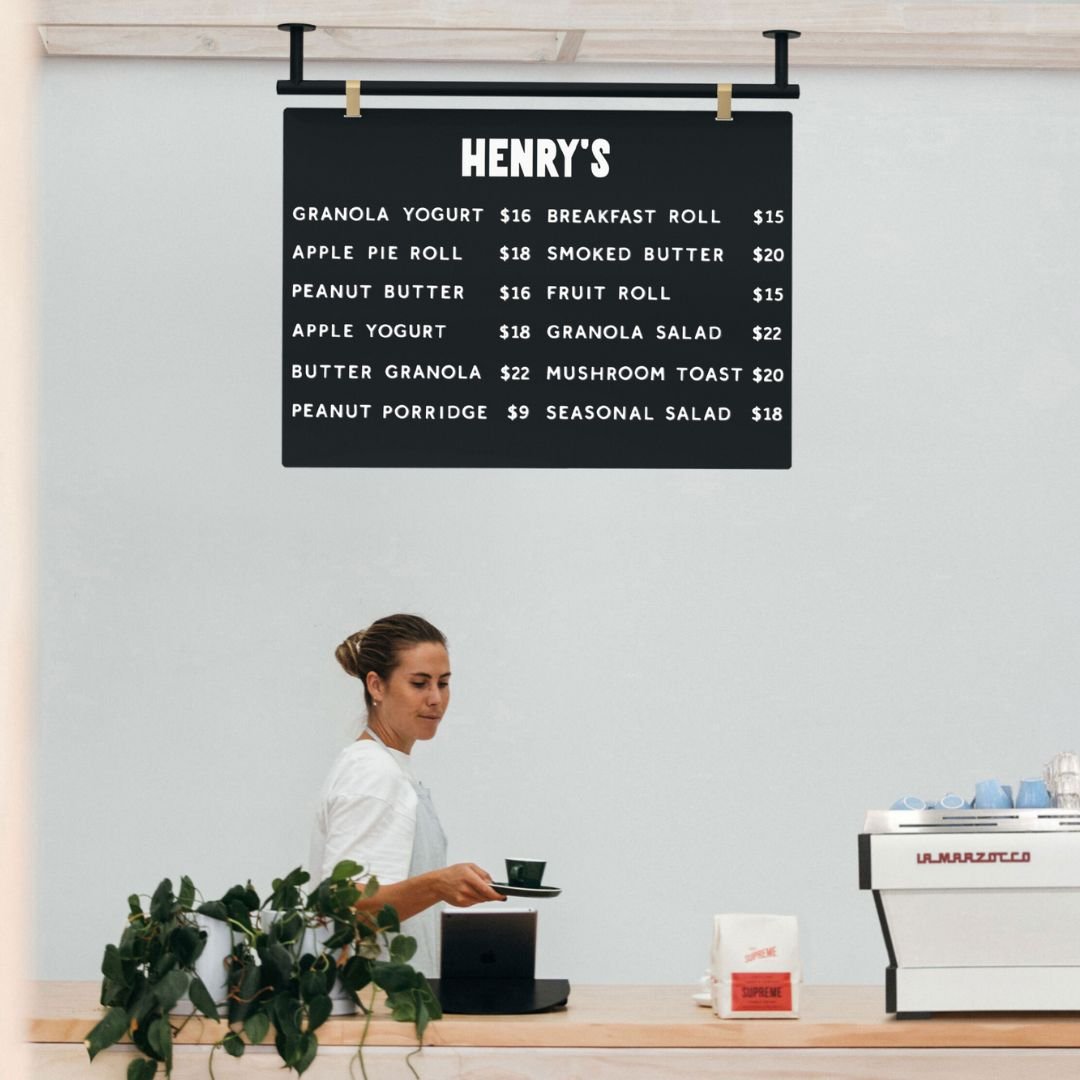 black ceiling menu board suspended from wooden beams behind a countertop with staff member walking underneath