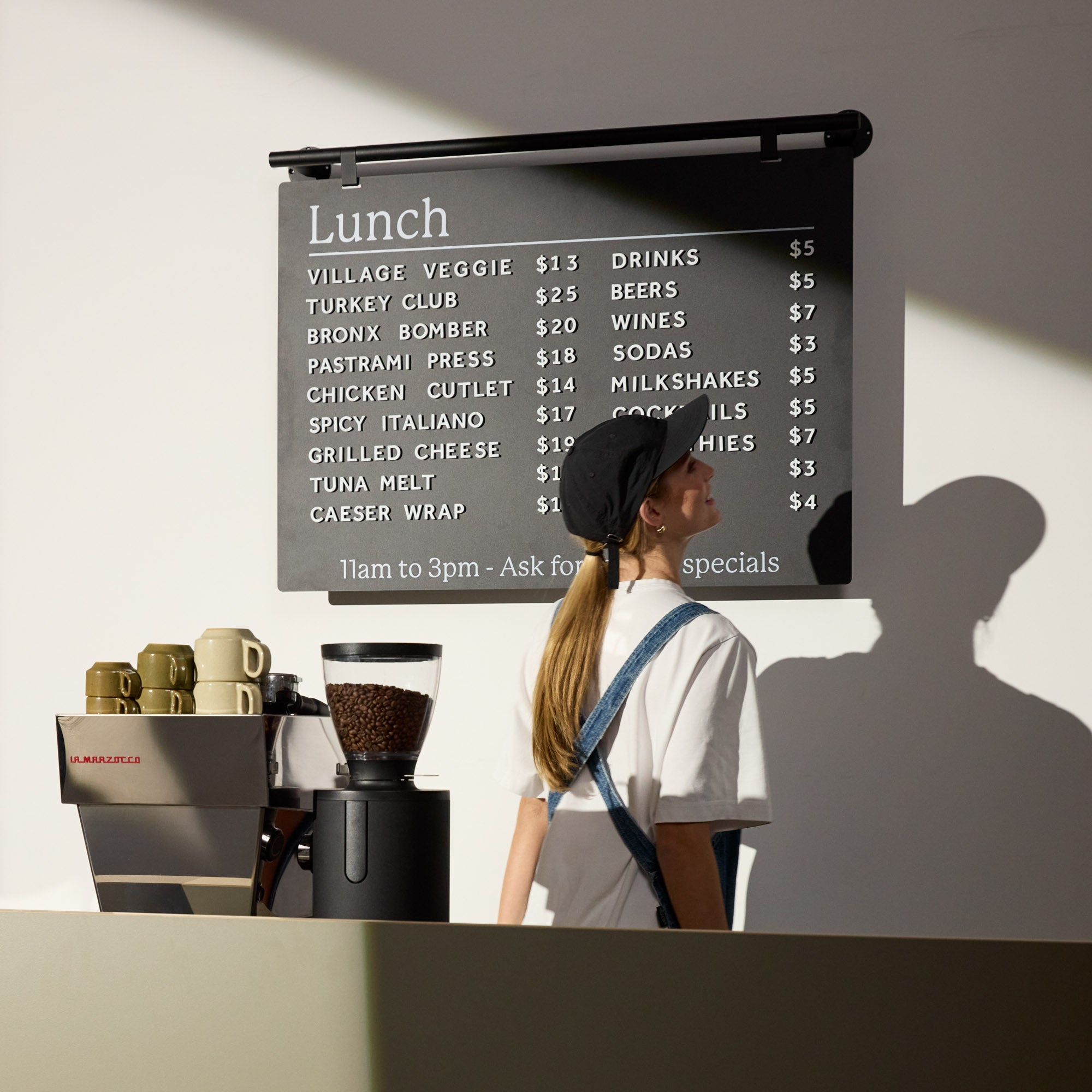 black ceiling menu board mounted onto a wall behind a countertop with staff member in front