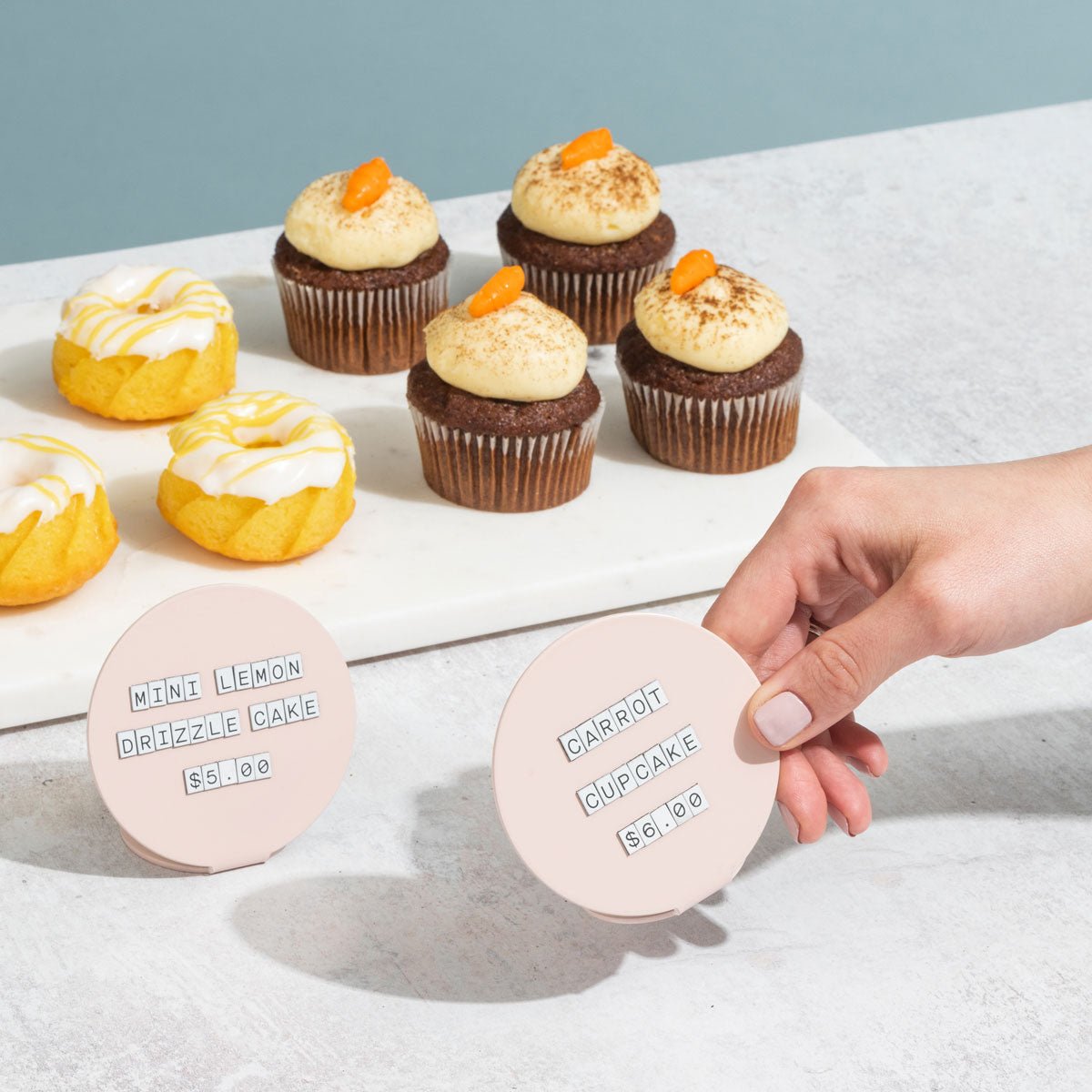 hand holding up a pink circle counter sign in front of a tray of pastries