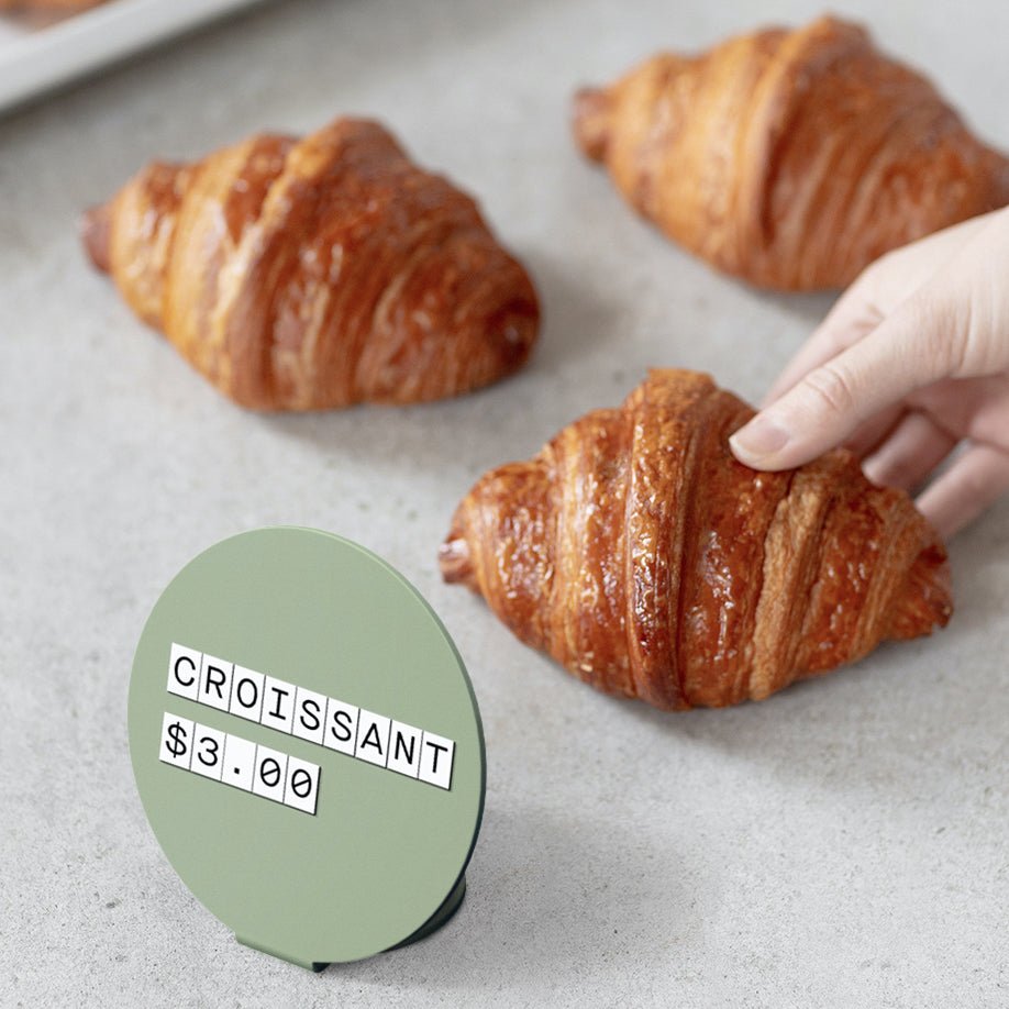 green circle counter sign used as a retail pricing display in front of row of pastries