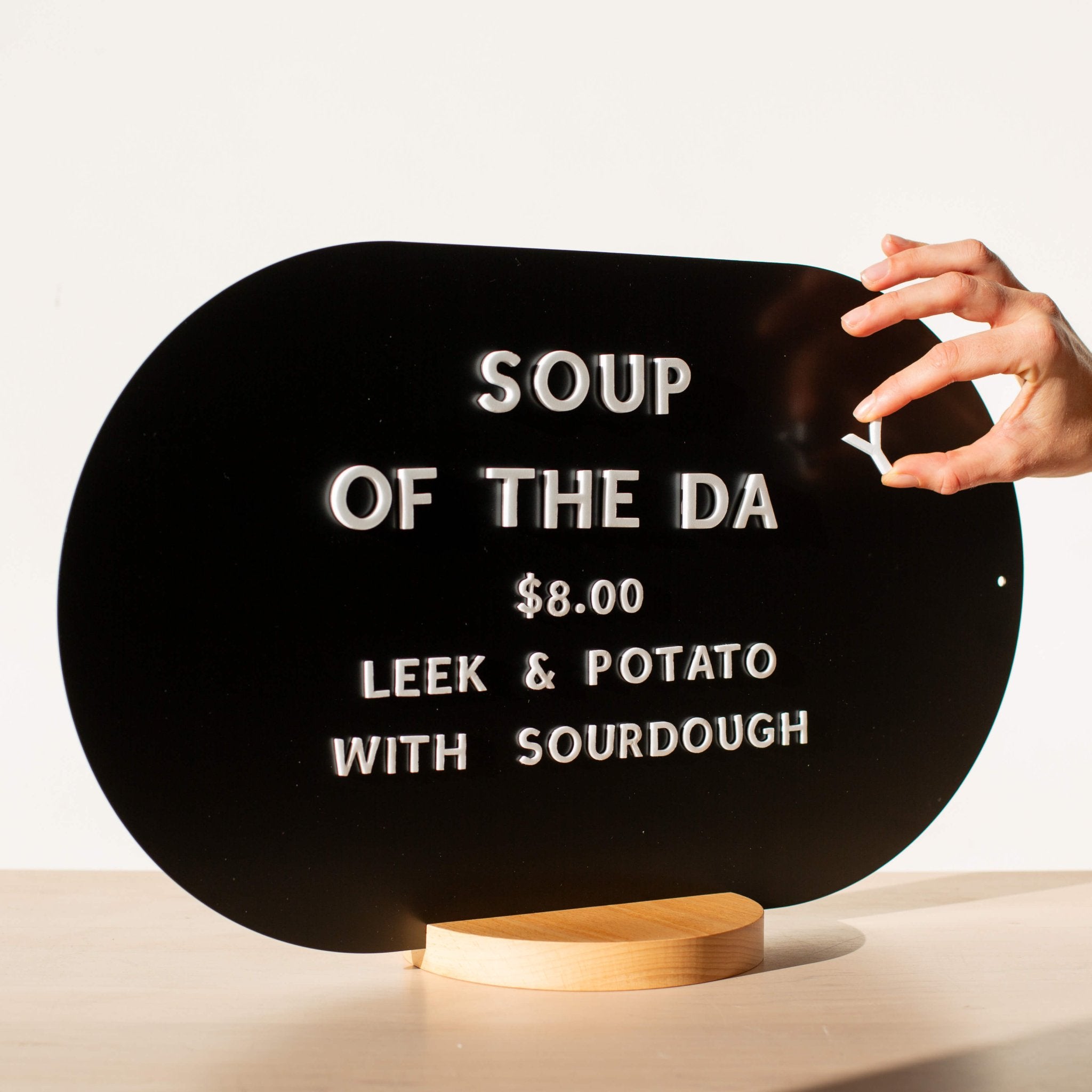 close up of the black curve tabletop menu display with a hand adjusting white magnet letters