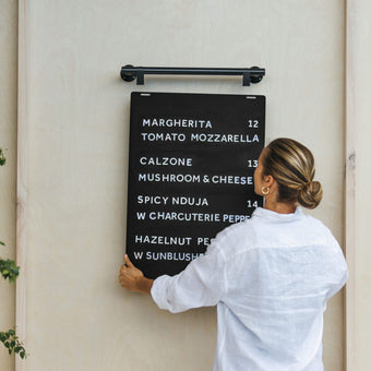 person lifting a black hanging menu board onto the hooks mounted on the wall