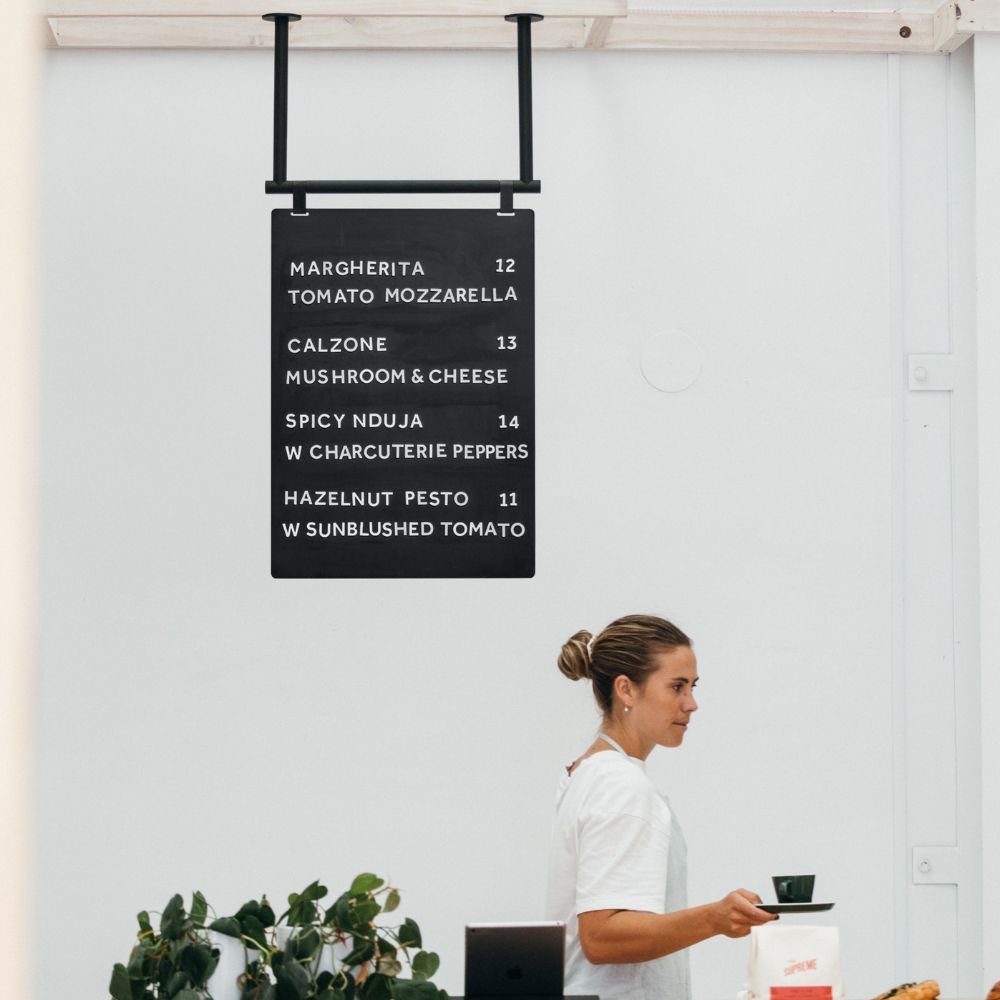 black hanging menu board using extension rods suspended from a tall bar on the ceiling behind a countertop