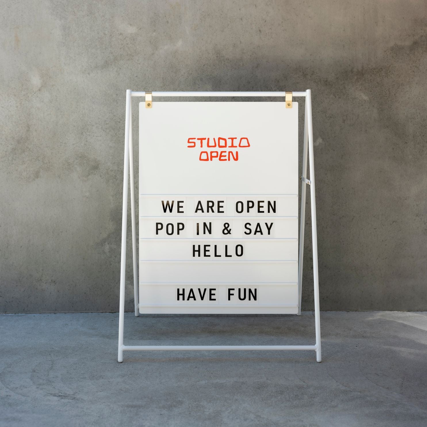 white large letter sidewalk sandwich board sign in front of a concrete wall with welcome message displayed