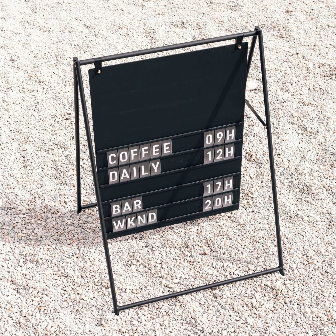 black large letter a-frame sidewalk sign on gravel with opening hours displayed