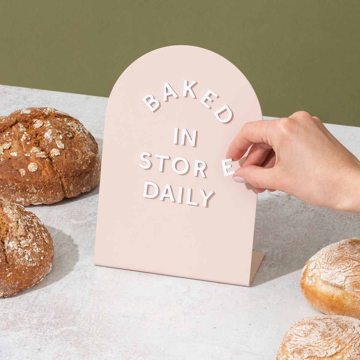 a hand adjusting the magnet letters on a pink table talker counter sign