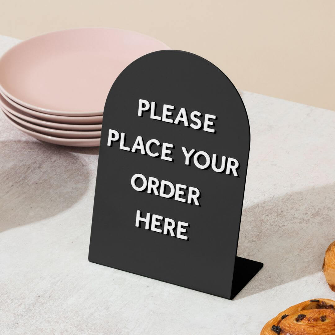 large round black table talker counter sign with "please place order here" on it in magnet letters