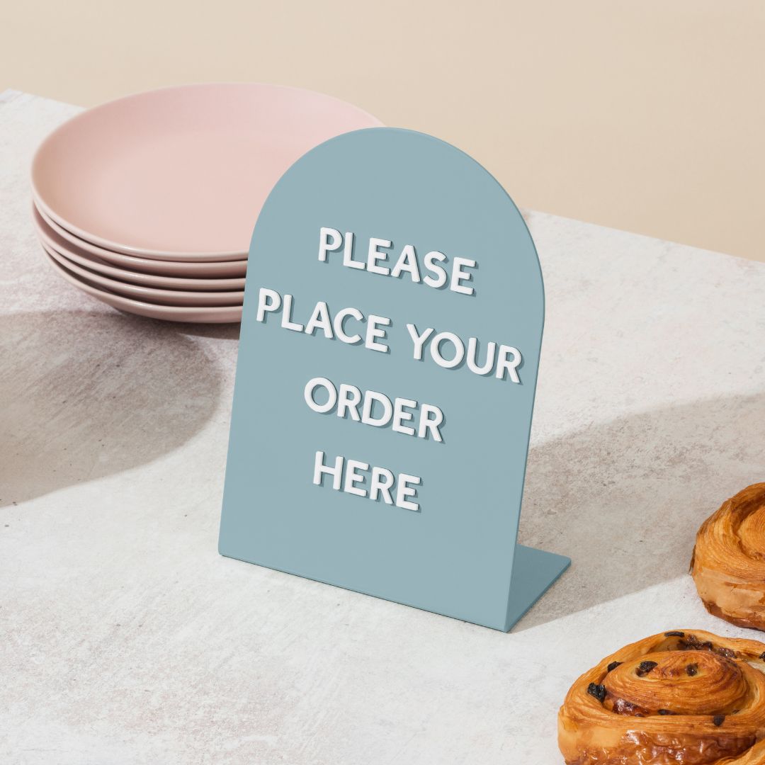 large round blue table talker counter sign with "please place order here" on it in magnet letters