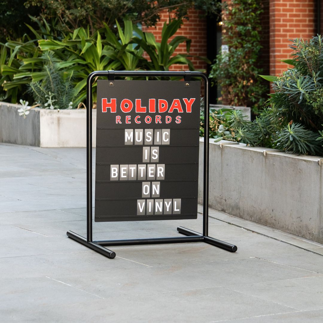 black letter sandwich board sign on sidewalk with red branding applied and displaying welcome message