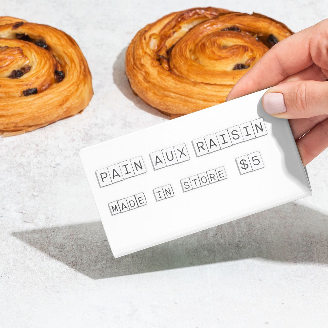 hand picking up the white medium counter sign showing pastry flavour and pricing