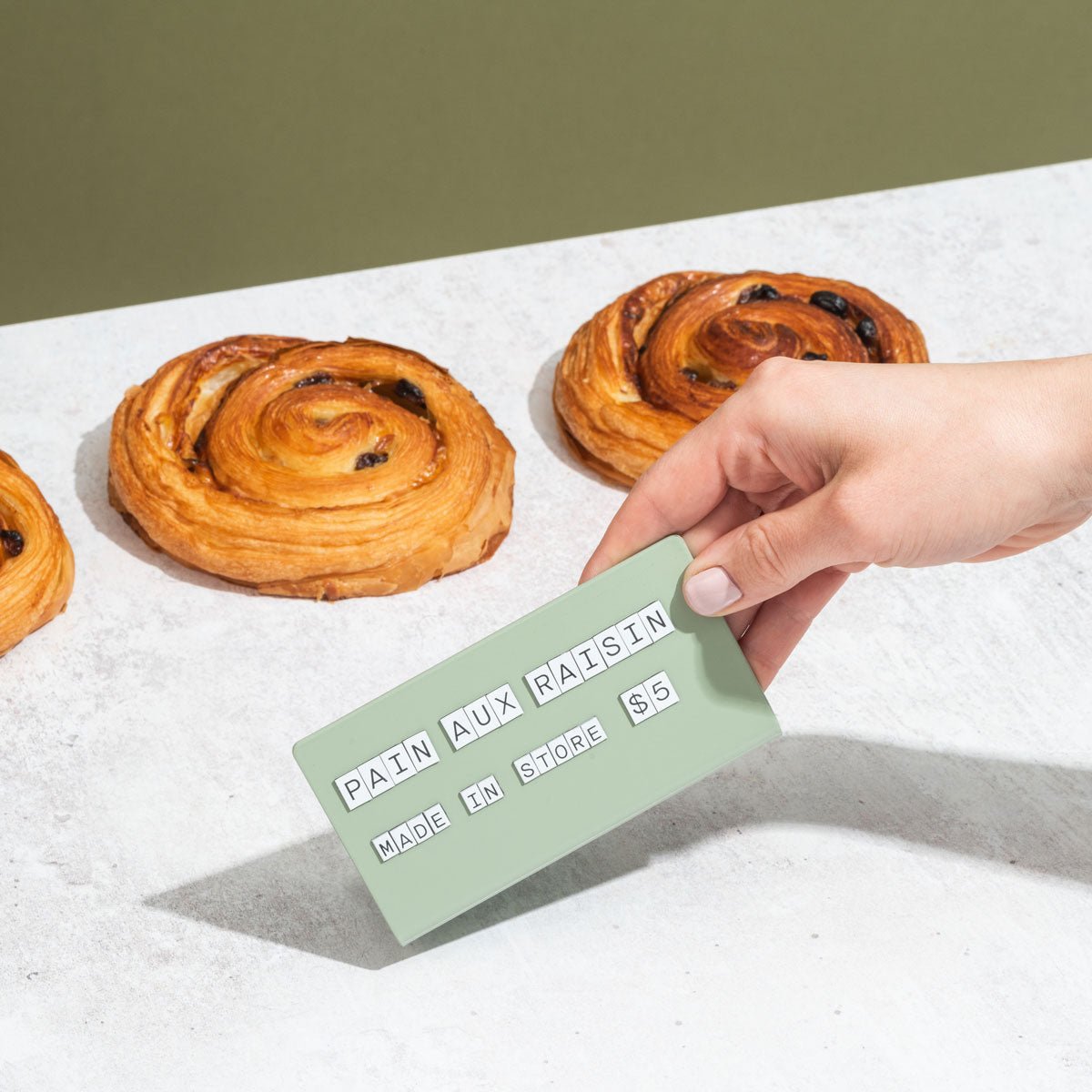 hand picking up the sage medium counter sign showing pastry flavour and pricing