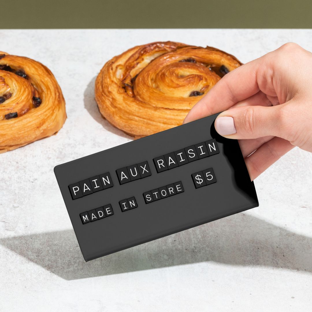 hand picking up the black medium counter sign showing pastry flavour and pricing