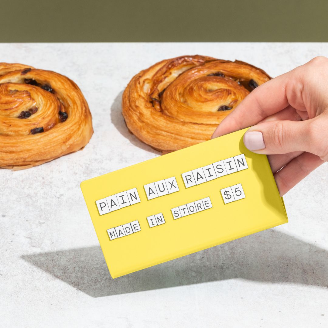 hand picking up the yellow medium counter sign showing pastry flavour and pricing