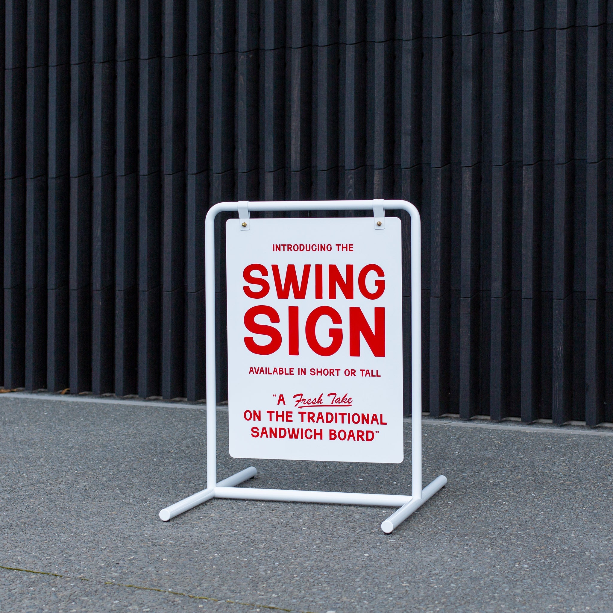 white swinging style metal signage in front of a shed on pavement with red logo branding