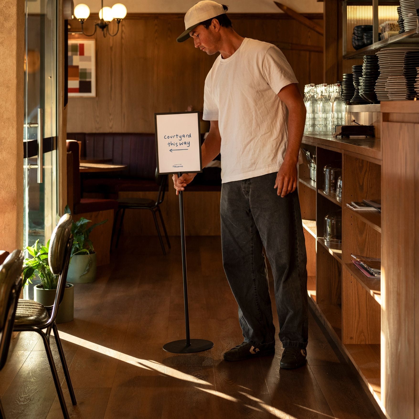 person lifting a metal black standing sign holder inside a restaurant showing wait here to be seated message
