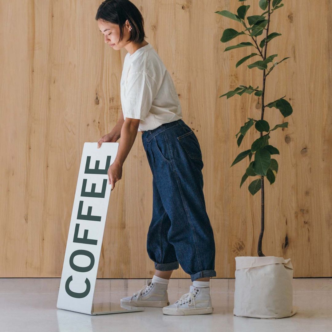 person putting out a metal sidewalk welcome sign with "COFFEE" on it