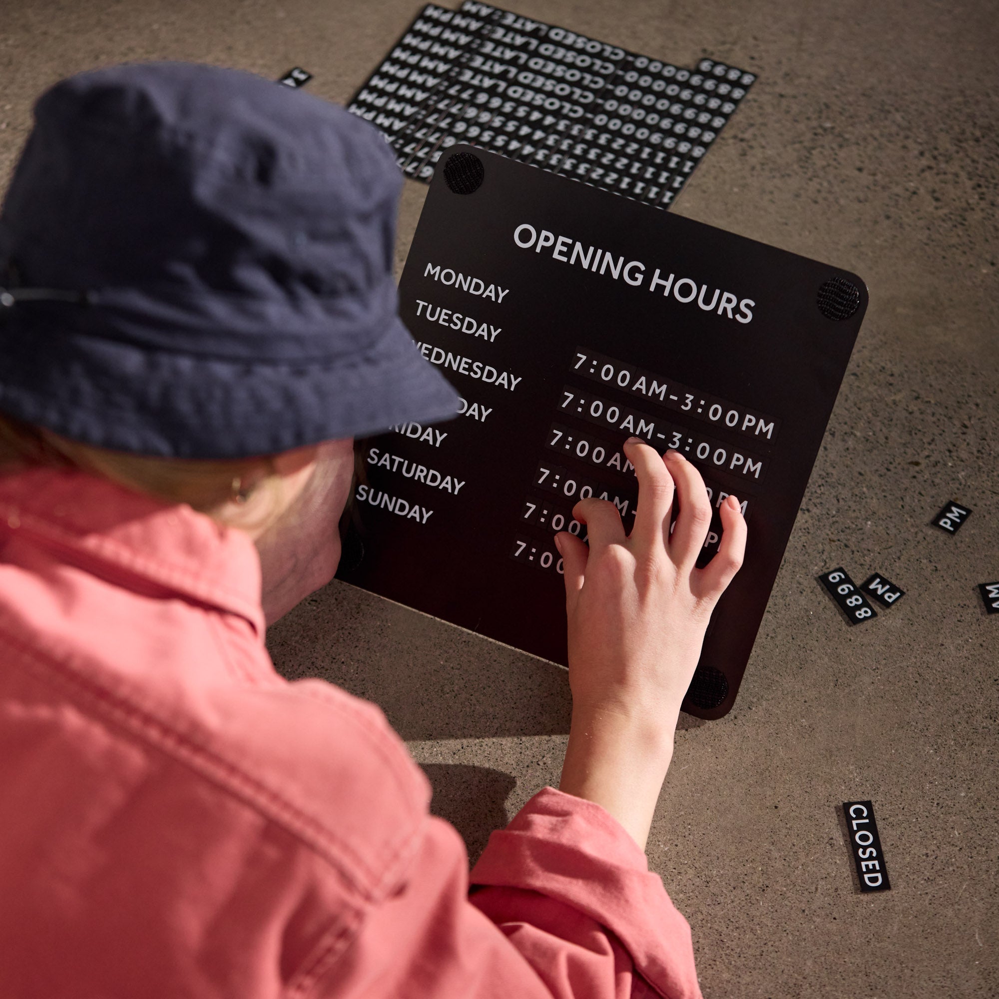 Magnetic numbers being applied to black Opening Hours Sign for window to show hours of operation