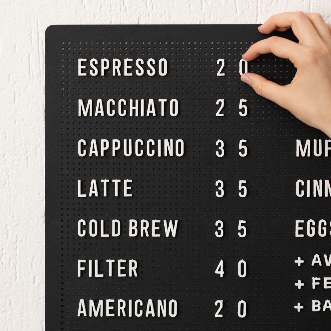 Close-up of hand placing white letters onto black peg letter board showing espresso menu