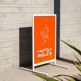 white framed poster sidewalk business sign outside against a wall on pavement with red poster inside