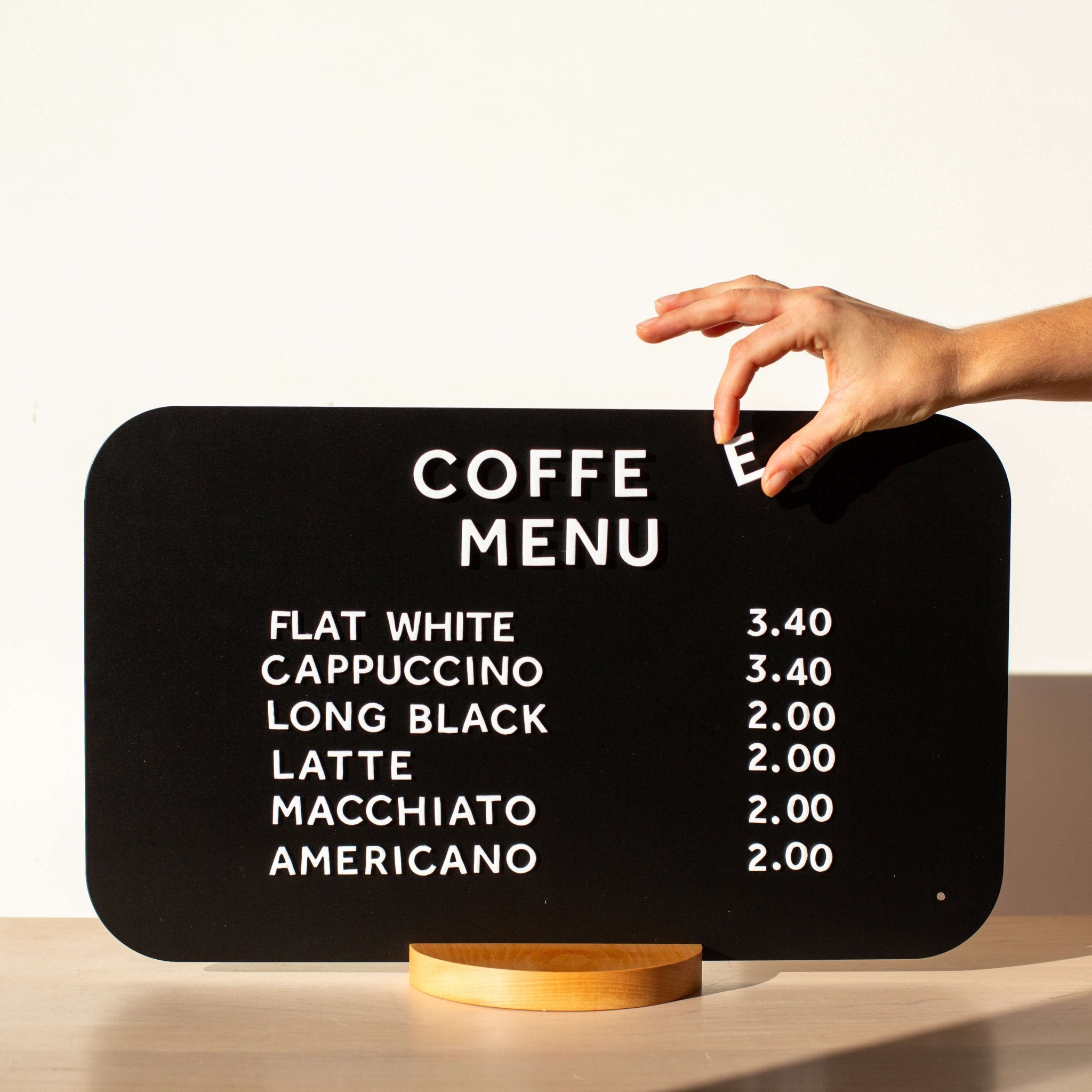 black rectangle tabletop sign displayed in horizontal orientation on a countertop with a hand changing the magnet letters
