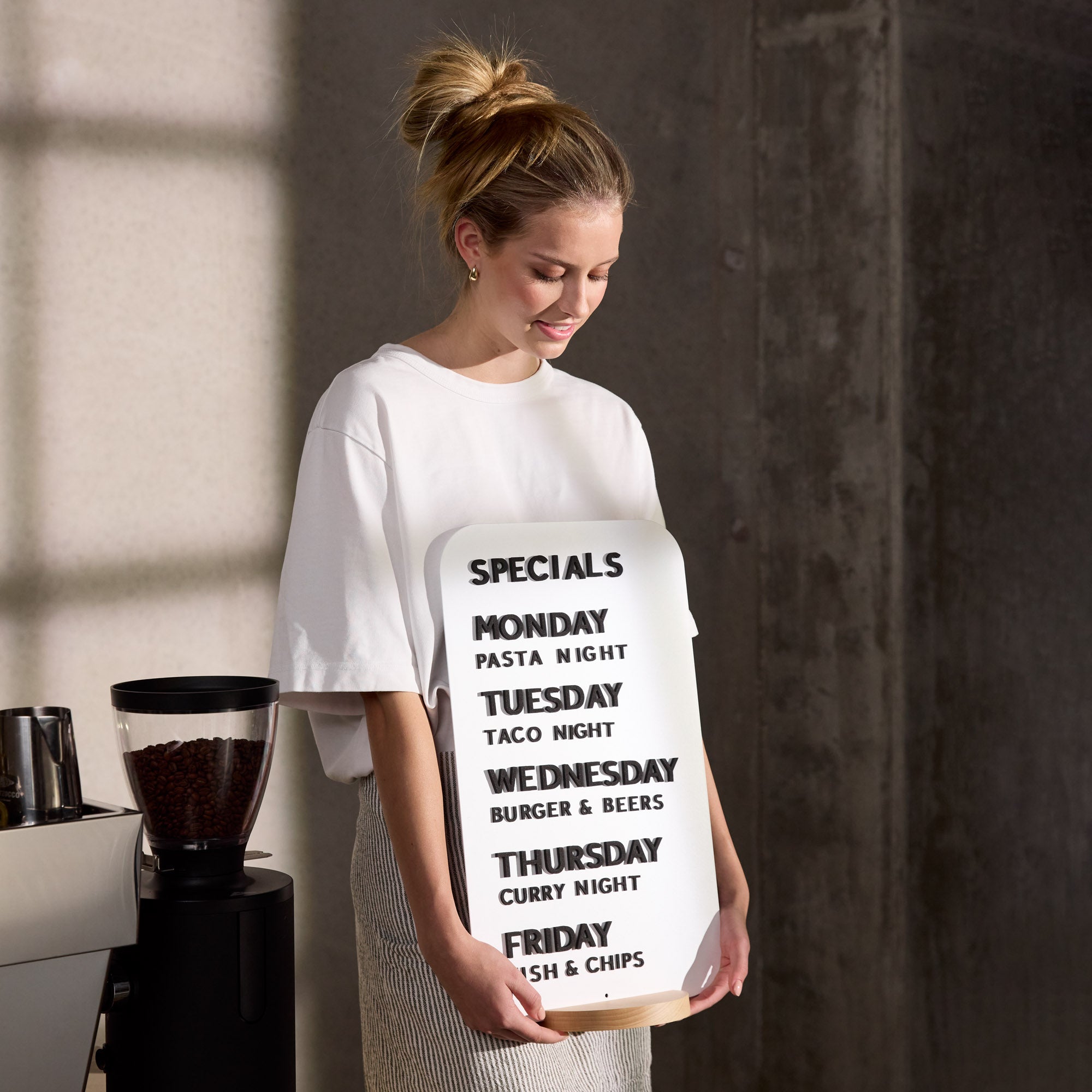 girl carrying a white rectangle tabletop sign with black magnet letters