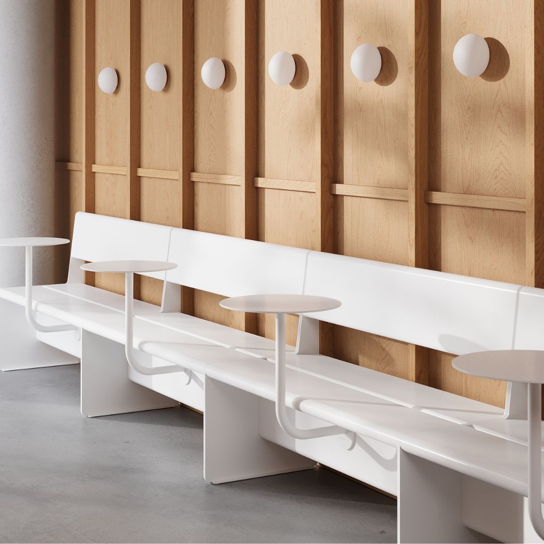 White cafe tables set up compactly in restaurant with bench seats and a wooden wall