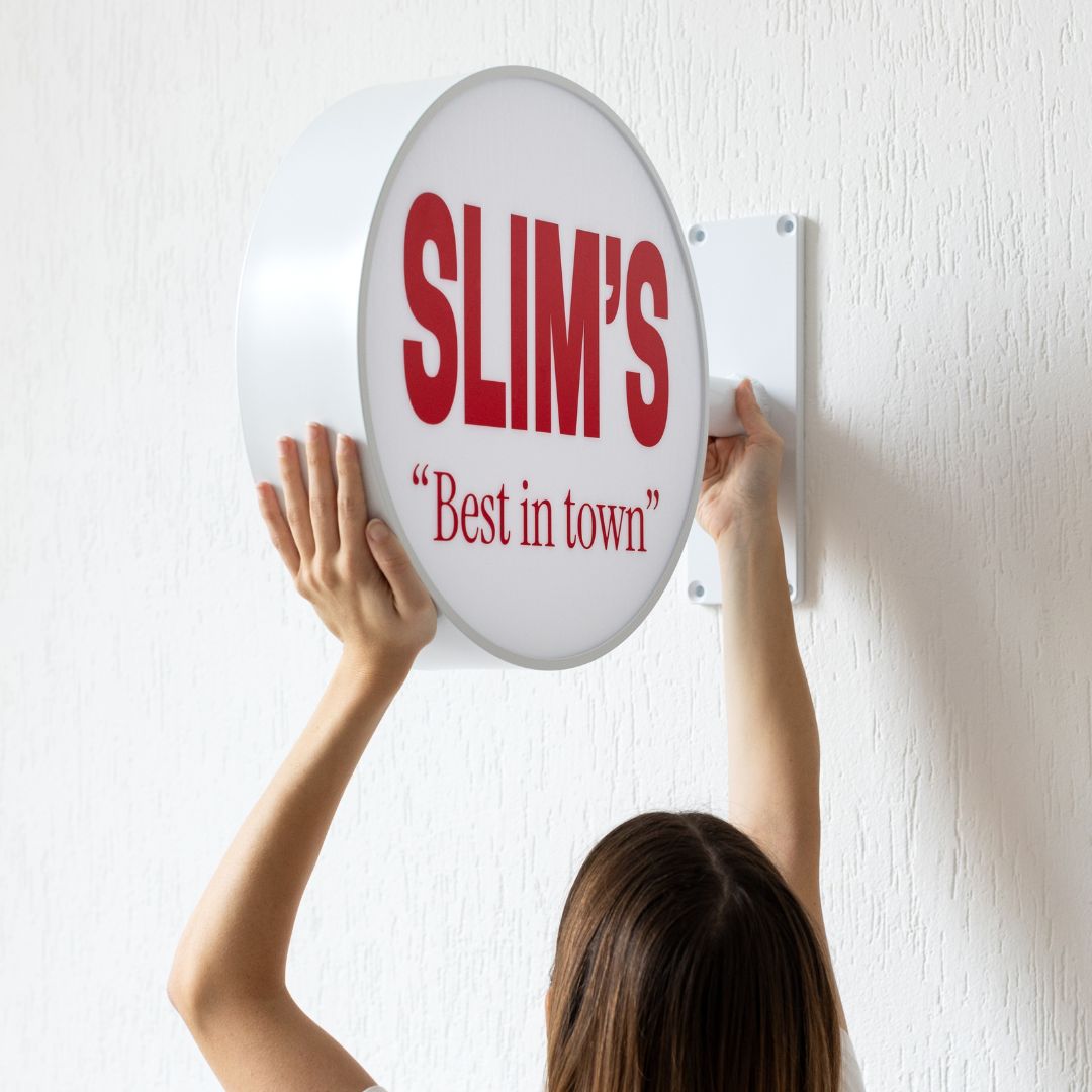 person holding and installing round light box wall sign on a wall