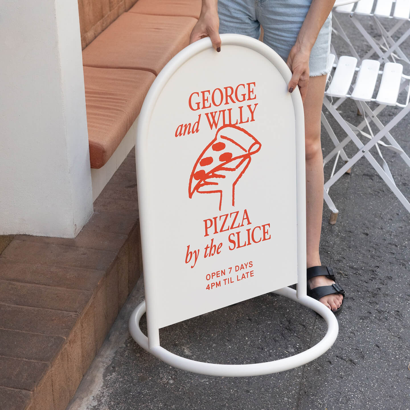 close up of a person lifting white rounded custom metal sign onto pavement outside business