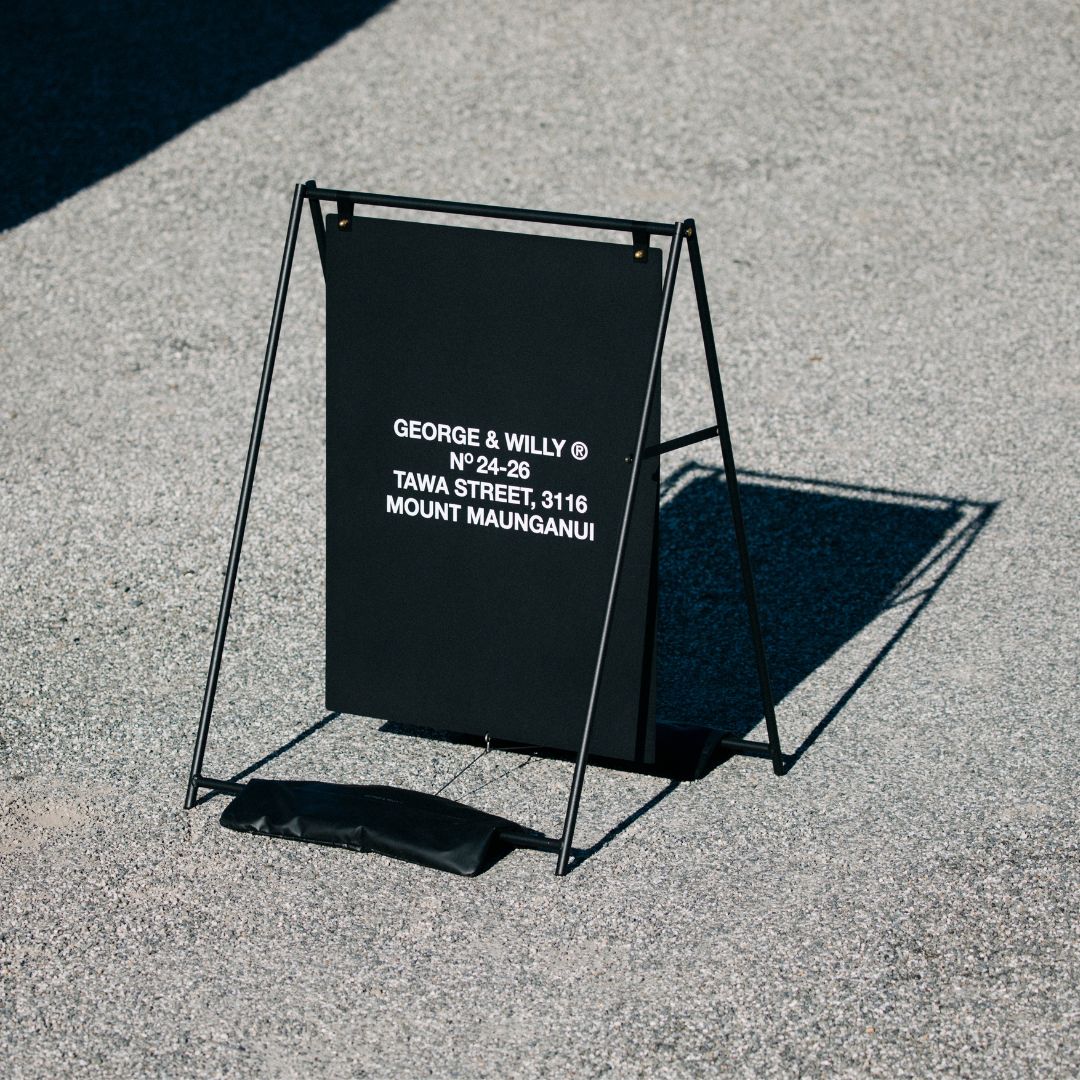 large a-frame sidewalk business sign with red logo on it using black sandbags