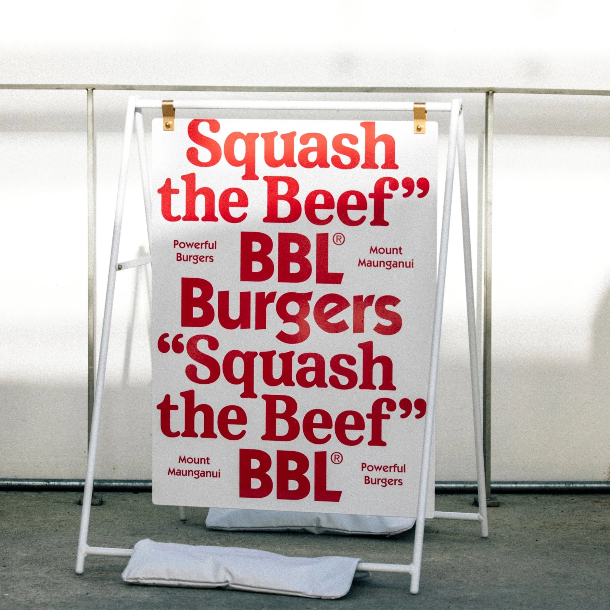 large a-frame sidewalk sign with red logo on it using white sandbags