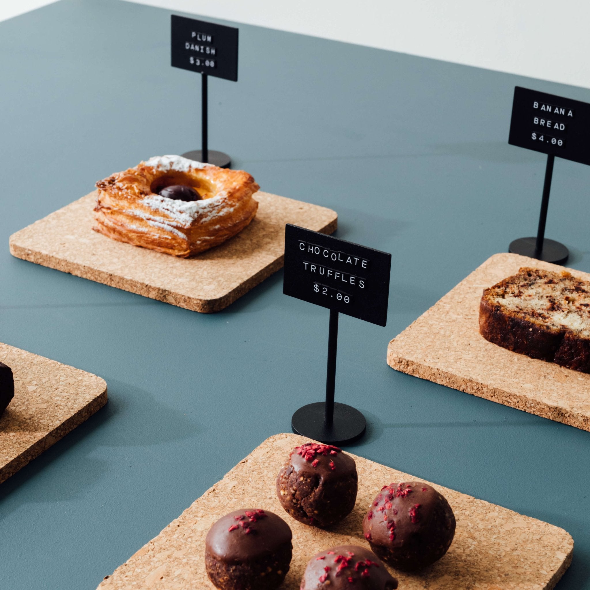 black standing counter signs in front of pastries and bakind showing prices