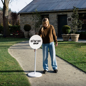 white round signs of advertising being placed on pavement by girl surrounded by grass