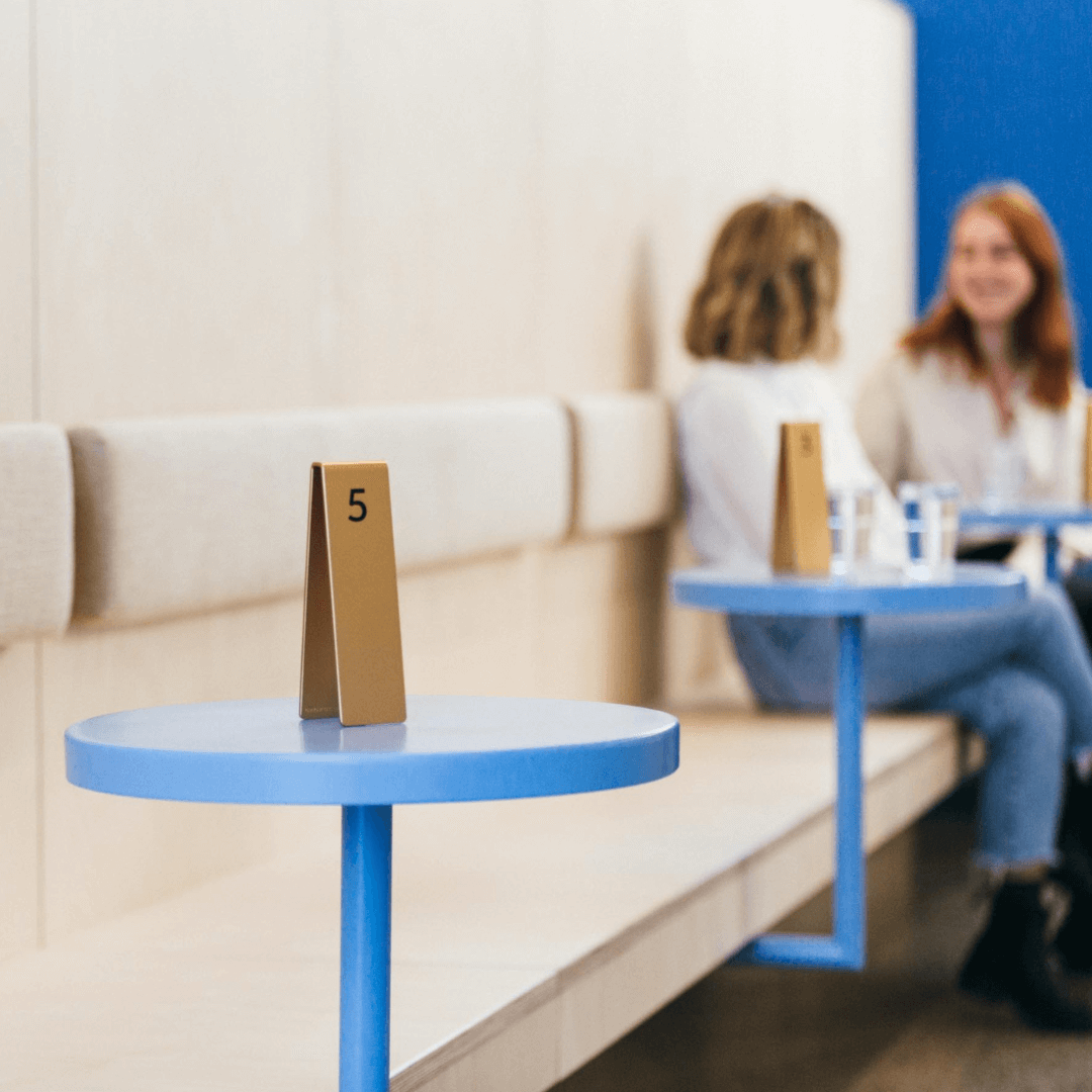 Metal triangle table number stacker on blue café table with customers seated in background