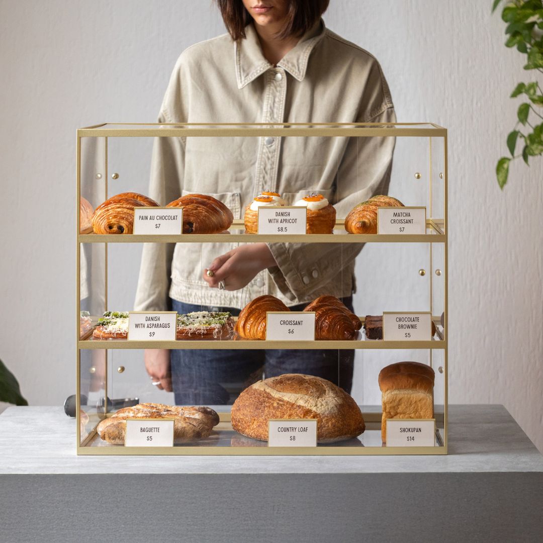 brass three-tier acrylic bakery display case with person opening the doors