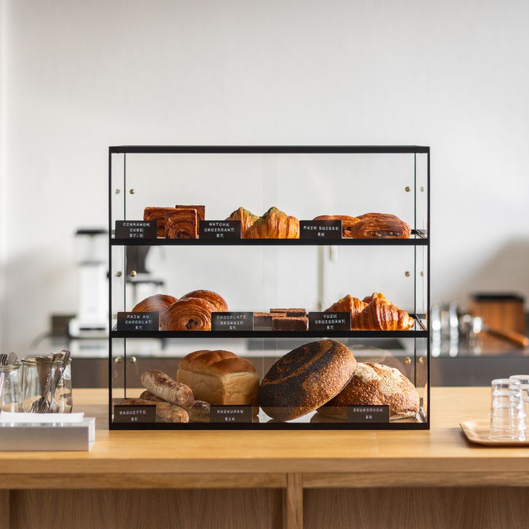 black three-tier bakery display case on a countertop filled with bread and pastries