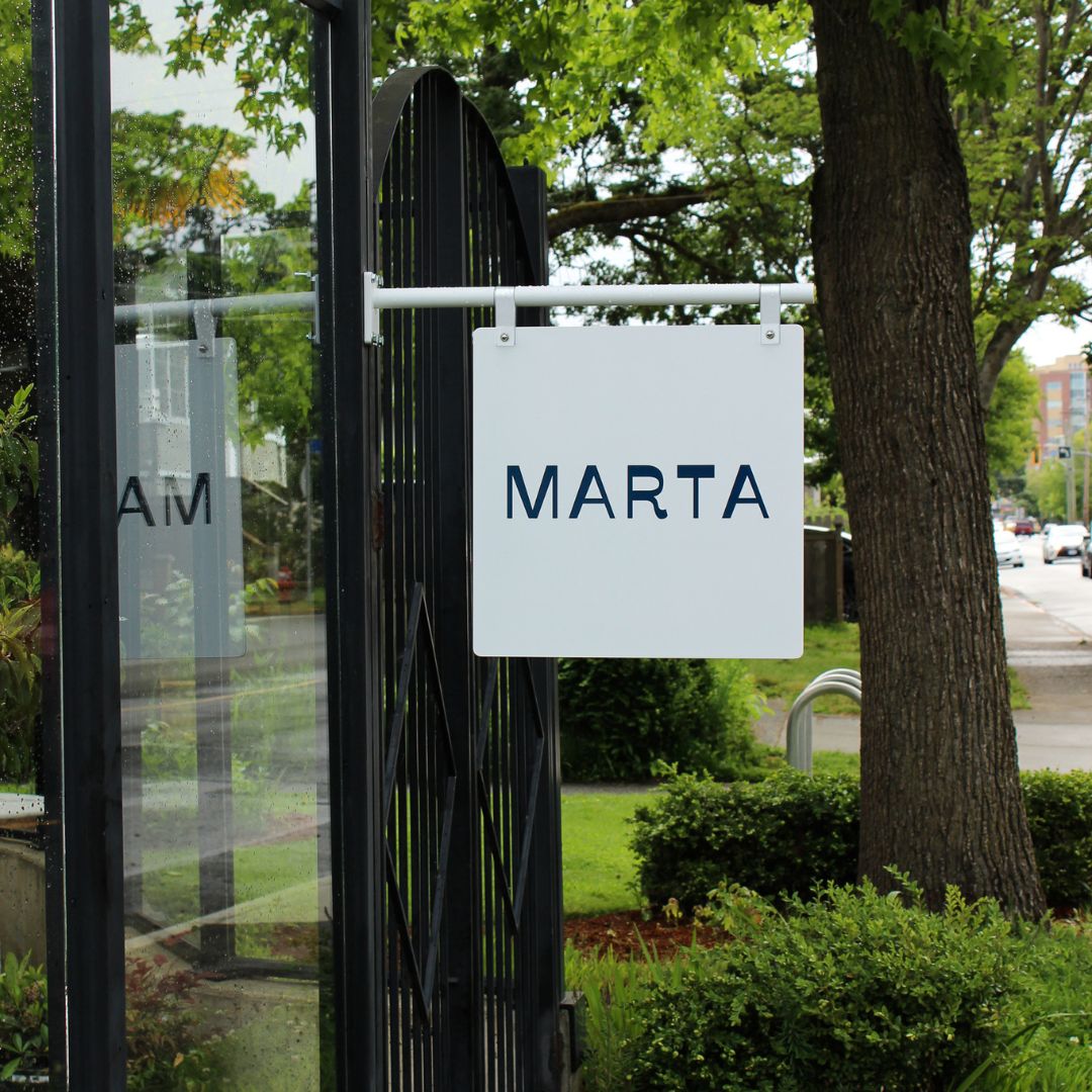 white hanging shopfront business sign installed against a shop brick facade