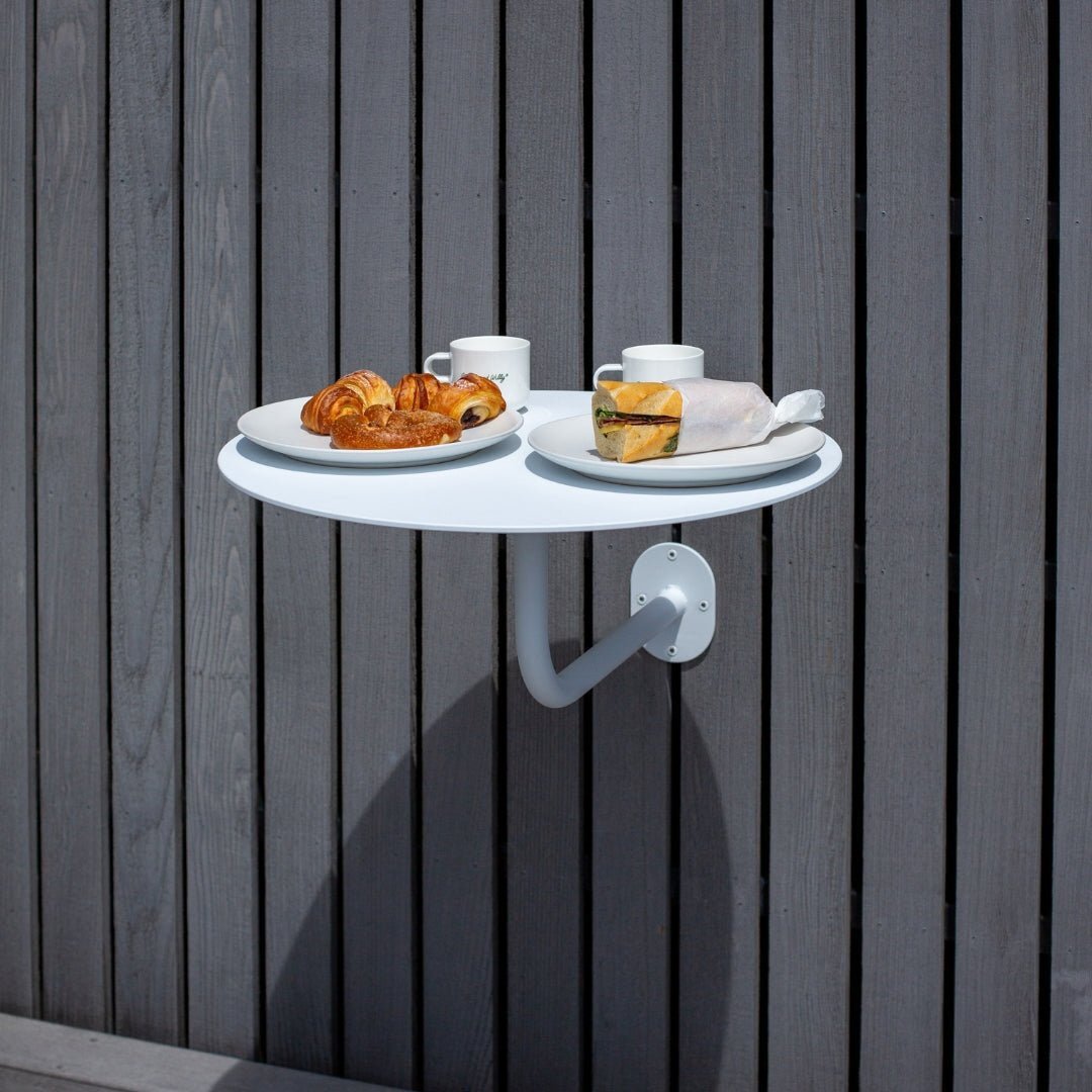 Large white round cafe table attached to wall with pastries and tea