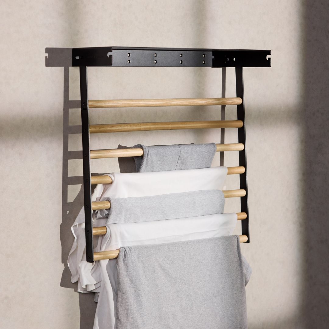 black wall mounted drying rack folded down with clothes hanging on it