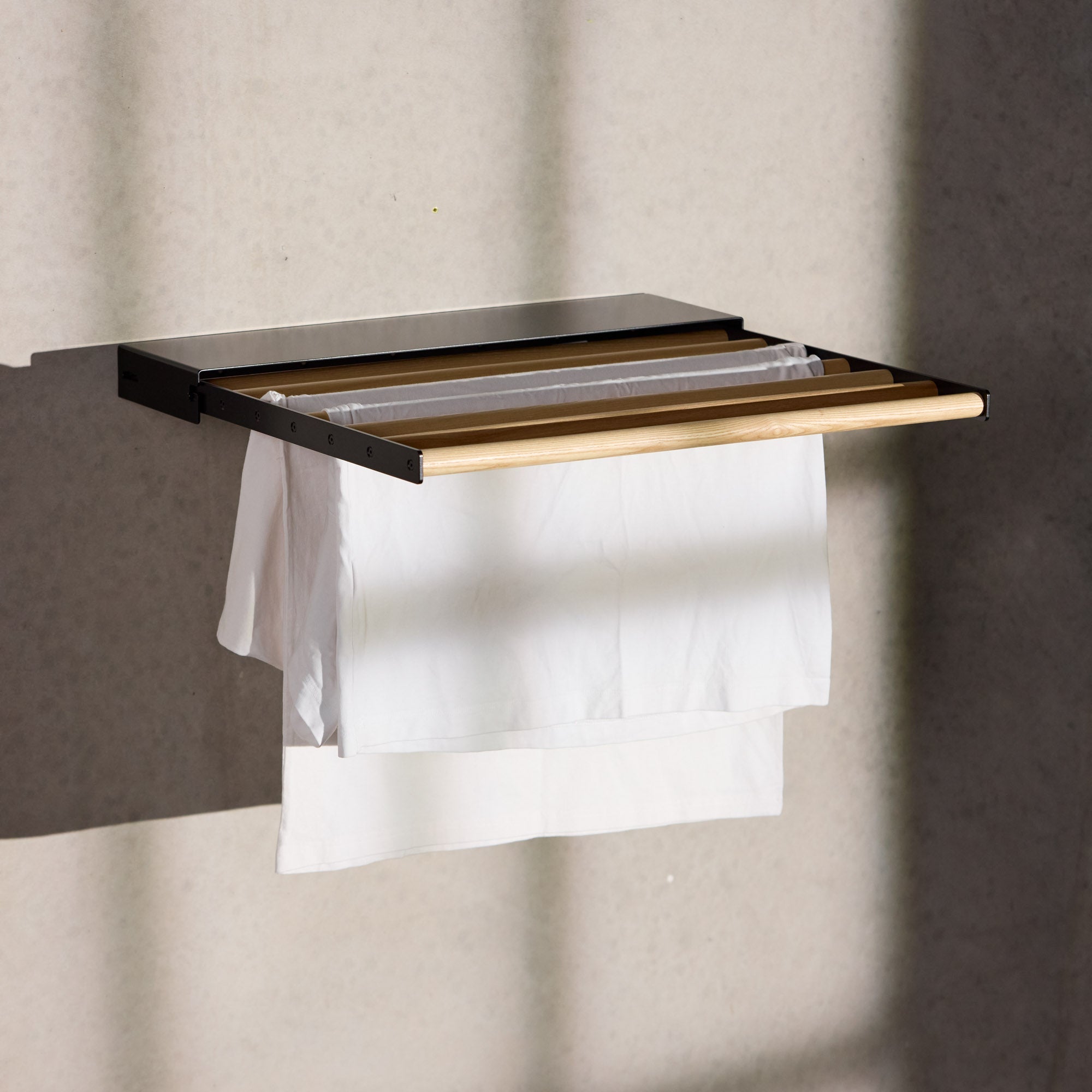 black wall mounted drying rack with clothes hanging on it with light shining through windows on it
