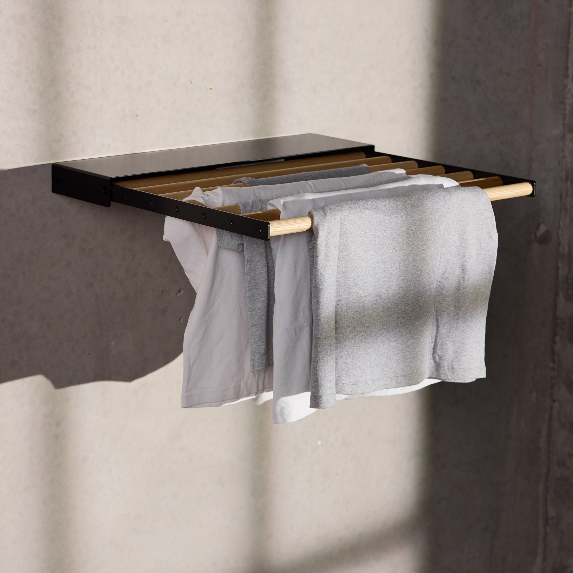 black wall mounted drying rack with clothes hanging on it with light shining through windows on it