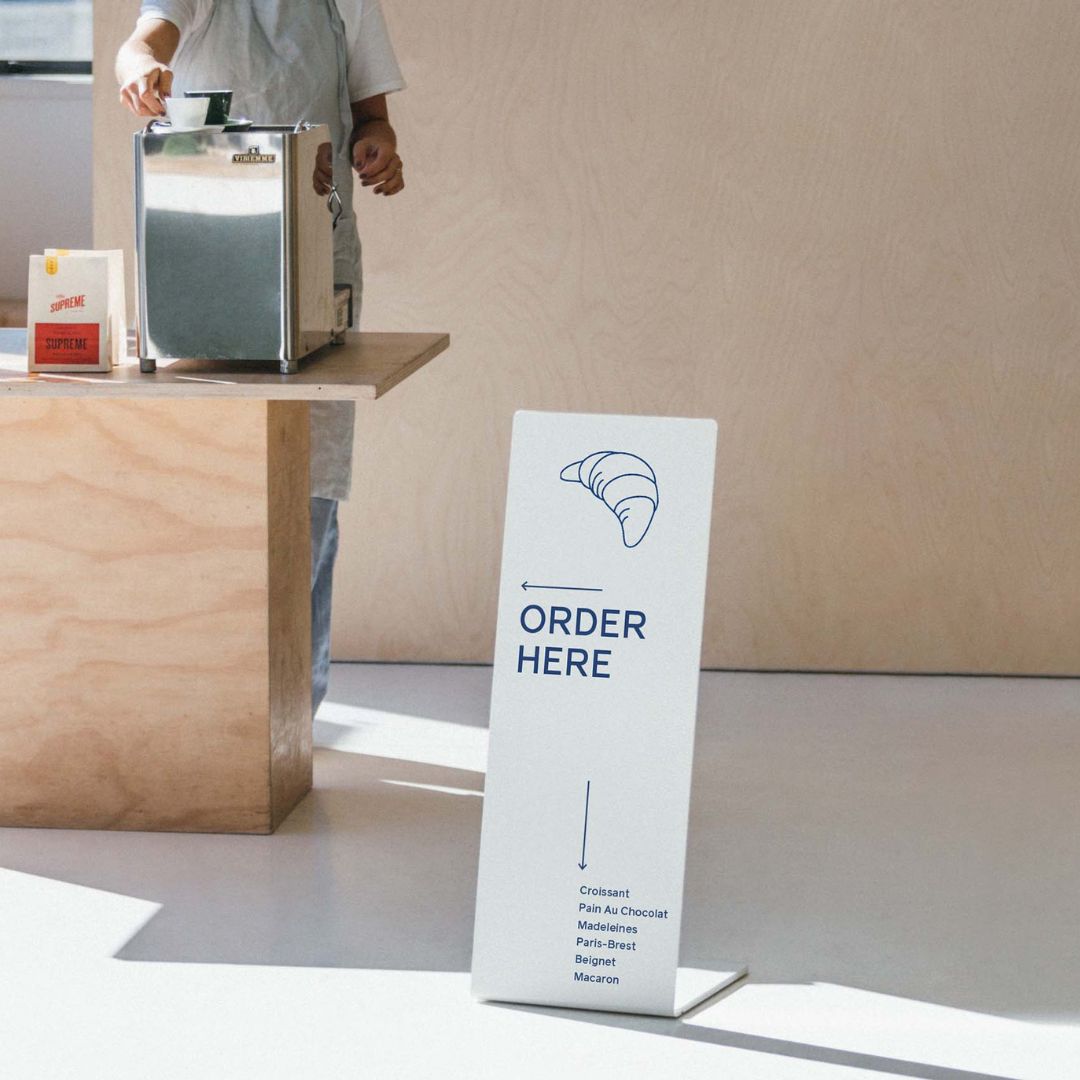 white welcome sidewalk metal sign in a cafe in front of a coffee bar counter