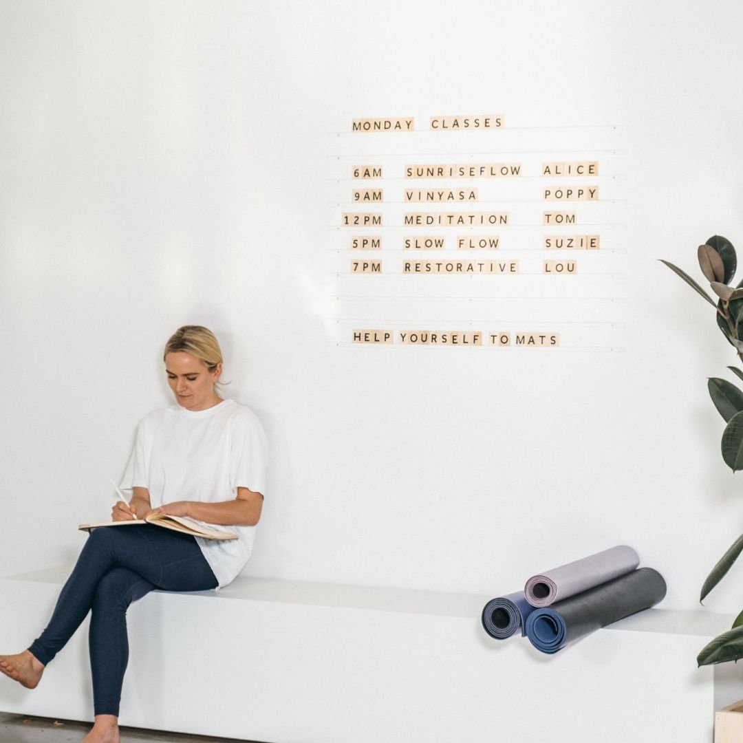 girl sitting on bench seat beside yoga mats underneath white wooden letter board rails with wooden letters