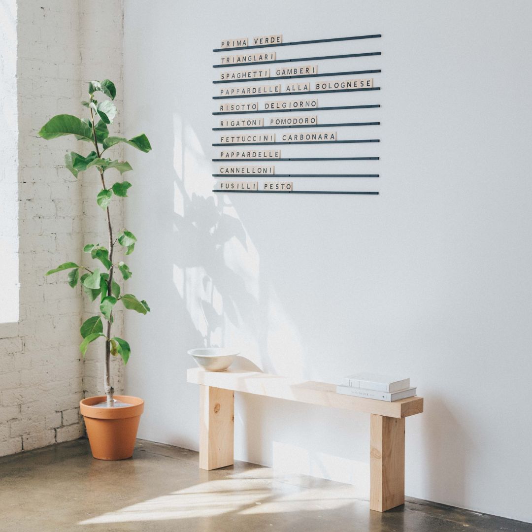 wooden letter board installed on a wall above bench seat beside a plant
