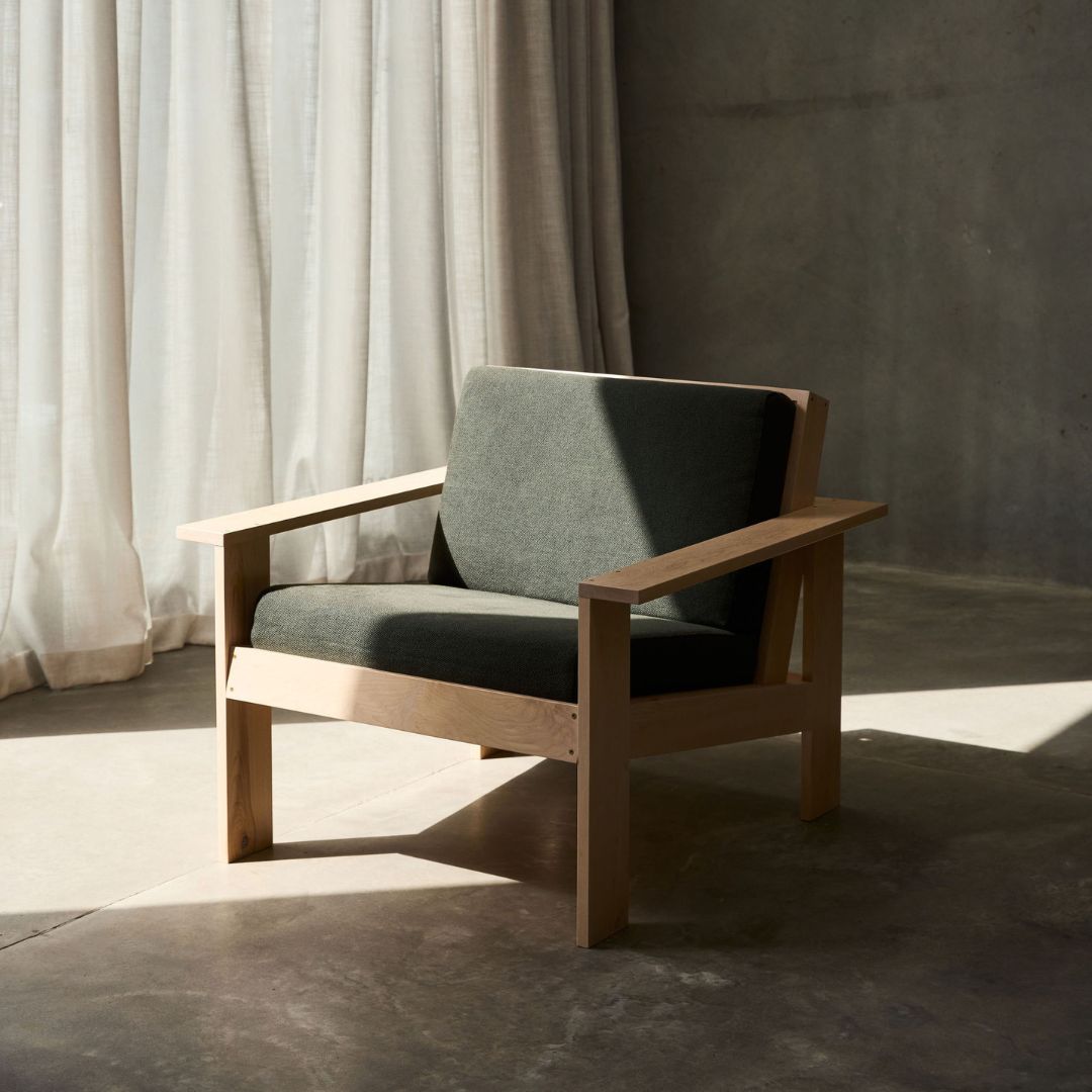 Wooden armchair with green cushion in a room with curtains and concrete wall.