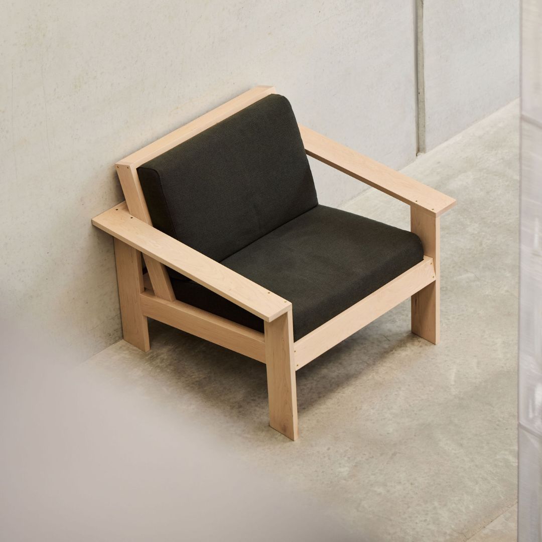 Minimalist arm chair with black cushions and wooden frame on a neutral background